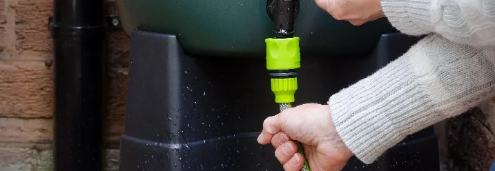 Person schließt Schlauch an Regentonne an